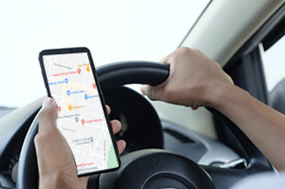 Imagem da notícia imagem foca no volante de um veículo e nas mãos do motorista. Com uma das mãos ele dirige e com a outra navega por um sistema de GPS em seu smartphone.