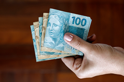 Ir para Imagem da notícia Imagem de notas de 100 reais dobradas em mão feminina