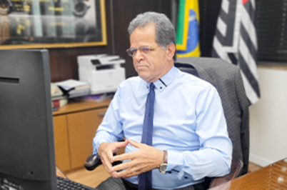 Imagem da notícia Valdir Florindo, desembargador-presidente do TRT-2, concede entrevista na modalidade remota para Jota. Ele tem cabelos grisalhos, camisa azul clara e gravata azul marinho. Em segundo plano, as bandeiras do estado de são paulo e do Brasil em seu gabinete.