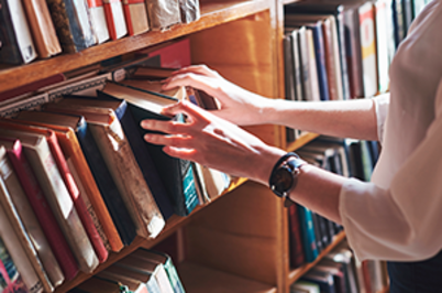 Imagem da notícia Imagem de mãos femininas mexendo em livros em estante de madeira