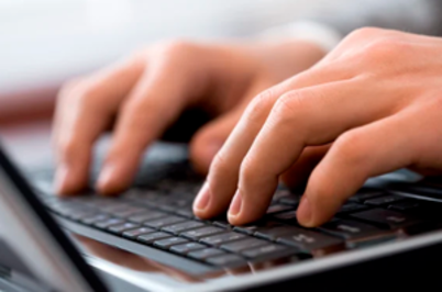 Imagem da notícia A imagem mostra um close-up das mãos de uma pessoa digitando em um teclado de notebook. Os dedos estão posicionados sobre as teclas pretas, e o foco está nas mãos, com o fundo levemente desfocado, sugerindo um ambiente interno bem iluminado. As mãos parecem estar em movimento, indicando que a pessoa está ativamente digitando.