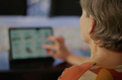 Imagem da notícia Imagem de mulher de cabelos curtos grisalhos, vista de costas, mexendo em tablet