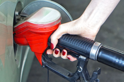 Imagem da notícia A imagem mostra uma mão segurando uma bomba de combustível enquanto abastece um carro. A mão tem unhas pintadas de vermelho, e o bico da bomba de combustível é preto com uma proteção vermelha. O veículo que está sendo abastecido é de cor verde clara. A cena parece estar ocorrendo em um posto de combustível.