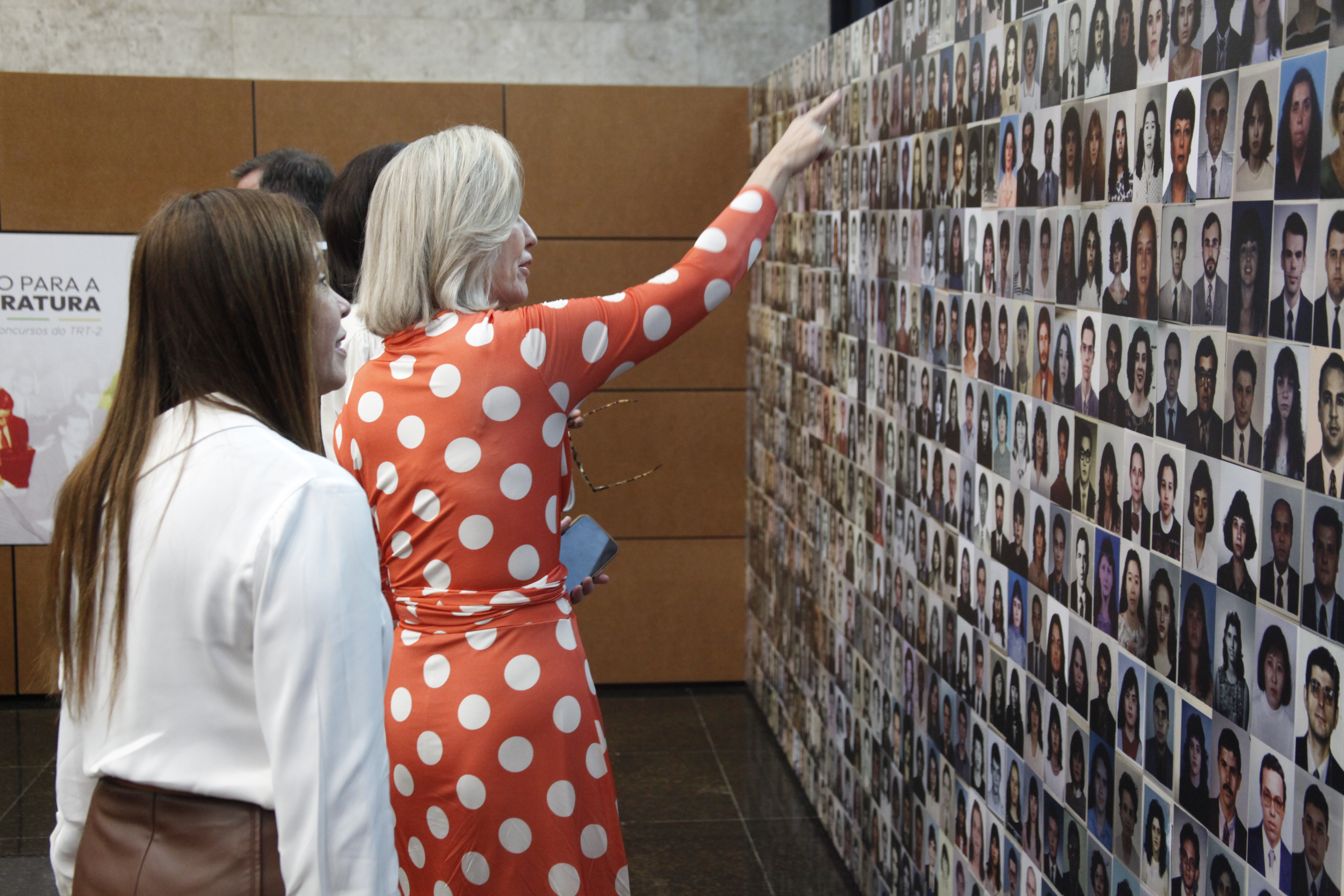 Mulher aponta para painel de fotos colado à parede