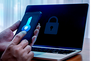 Ir para  Imagem da Notícia Imagem de mãos mexendo em um celular com notebook aberto ao fundo