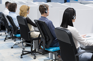 Imagem da Notícia Imagem de quatro pessoas sentadas de costas usando headphone em mesas de trabalho