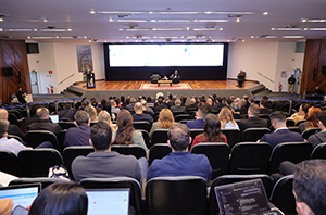 Imagem da Notícia Plateia vista de costas durante fórum de governança; ao fundo, o palco principal