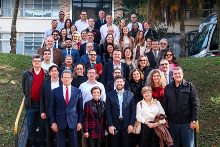 Imagem da Notícia Fotografia colorida de cerca de 35 magistrados dos TRTs da 2ª e 15ª Regiões reunidos em uma escadaria externa durante visita técnica à fábrica da Volkswagen em São Bernardo do Campo. Em trajes formais e casacos escuros, homens e mulheres sorriem para a foto organizados em fileiras, ladeados por um gramado verde com corrimão amarelo.