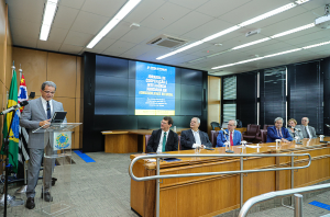 Imagem da Notícia Presidente Valdir Florindo discursando em púlpito no TRT, com autoridades à mesa e tela ao fundo sobre "Jornada de Inteligência Artificial"