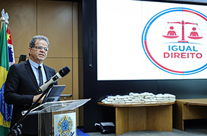 Imagem da Notícia Presidente do TRT-2 discursa em um púlpito com microfone. Ao fundo, uma grande tela exibe a marca do projeto "IGUAL DIREITO".