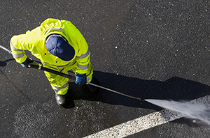 Imagem da Notícia Foto com vista de cima de gari limpando uma rua com jato d'água